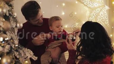 年轻、美丽的母亲、英俊的父亲和可爱的微笑的<strong>婴儿</strong>儿子在圣诞树旁的父亲<strong>怀抱</strong>中幸福的家庭